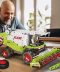 Man assembling Claas Lexion 760 Remote Controlled Combine Harvester Building Blocks Kit MOC with 1400+ pieces on table.