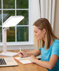 Woman using 10000 Lux Therapy Lamp For Mood And Energy Boost at desk, ideal for sunlight deprivation at home or office, white.