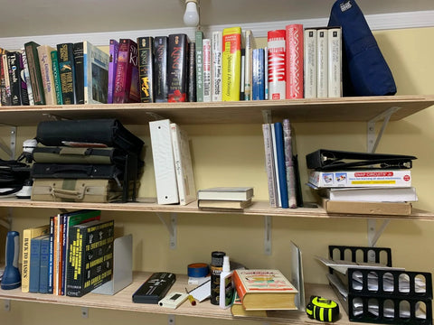Books and items on wood shelves supported by Heavy Duty 12-Inch By 8-Inch Shelf Brackets With 600 Lb Capacity 10 Pack White Metal L Supports.