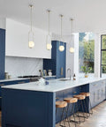 Modern kitchen with blue cabinets and four white pendant lights over island, large windows, and a marble countertop.