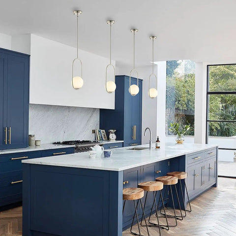 Modern kitchen with blue cabinets and four white pendant lights over island, large windows, and a marble countertop.
