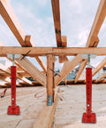 Two red adjustable basement floor jacks with screw threads supporting wooden framing