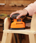 Electric Orbital Detail Sander Pumping Out 14000 OPM With Seamless Dust Collection on a wooden stool.