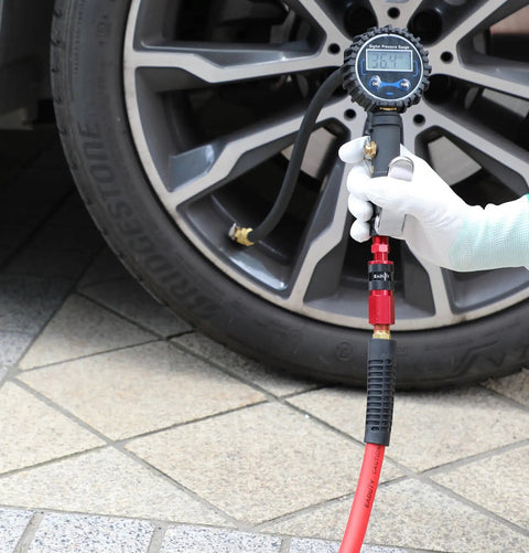 Slick Hybrid Air Compressor Hose 1/4 Inch By 25 Ft connected to tire pressure gauge near wheel in garage setting.