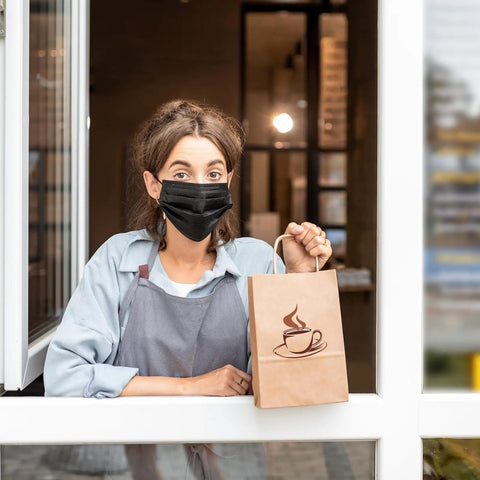 Person holding Bulk 150 Pack Brown Kraft Paper Gift Bags With Handles 5.25 x 3.2 x 8 Inches For Shopping Parties Weddings Birthday Merch