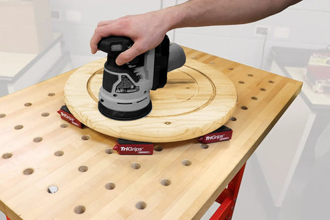 Triangle Bench Cookie Work Grippers 4 Pack Non Slip Project Supports For Woodworking And Painting Elevates Projects About 1.2 Inches On The Platform And 3 Inches With Built In Painting Supports For Edge Access And No Clamp Needed Setup showing a sander on wooden disc supported by red triangle grippers on a workbench.