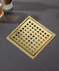 Gold square shower drain with mesh grille installed on dark tile floor