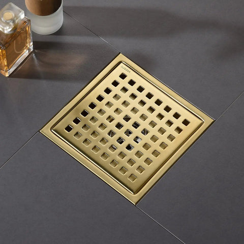Gold square shower drain with mesh grille installed on dark tile floor