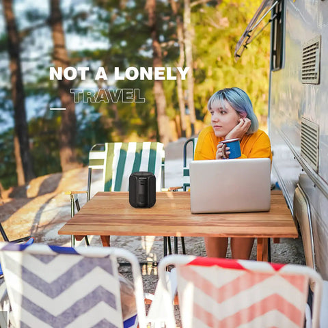 Person seated at outdoor table with a laptop and 15W Portable Bluetooth Speaker With Dual True Wireless Stereo For Party Vibe, Loud Crisp Highs And Deep Bass, IPX6 Waterproof Shower Speaker, Bluetooth 5.0, Dual Pairing For Home Theater And Gaming On The Go. Surrounded by trees and colorful chairs.