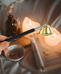 The Real Deal Copper Telescopic Bell Candle Fire Extinguisher With Hella Compact Retractable Design For Quick Flame Control and Solid Home Safety Shield Plus A Tight Little Knockout Gift For Any Kitchen Or Altar Setup, holding bell by lit candles.