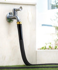 Garden hose, black with brass fittings attached to a chrome wall faucet