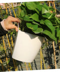 Person holding a white plastic pothos planter; part of Six Piece Wall Mounted Round Plastic Pothos Planters With Self Watering System For Indoor Balcony Gardens Hydroponic Hanging Flower Pots Set For Home And Office Decor.
