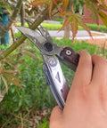 Person using 7 In 1 Garden Pruning Shears Folding Multitool With 8 Inch Professional Garden Scissors to prune a branch.