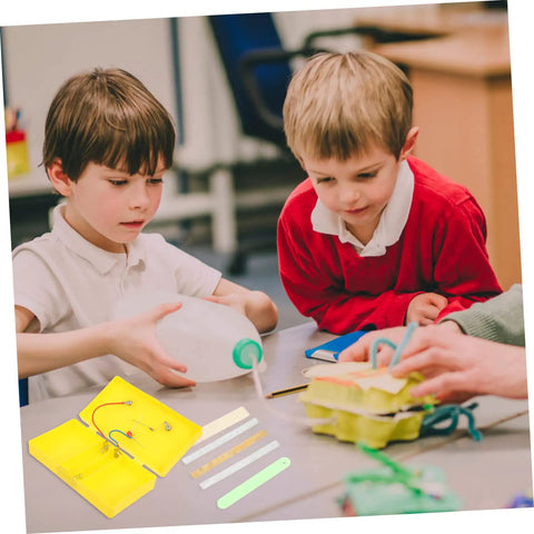 Two boys engaged with a yellow conductivity experiment kit, exploring electrical flow principles in a classroom.