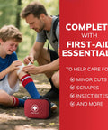 Red compact first-aid kit with white cross on forest ground as man tends a boy's knee.