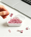 Hand holding a pink binder clip over a 12 Pack Cloud Paperclip Holder With Snug Lid Mini Plastic Desk Organizer with cloud design.