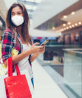Woman in mall wearing Filtering Barrier Face Covering AFFM-5 One Size 5-Pack with stretchable side bands, holding shopping bags.