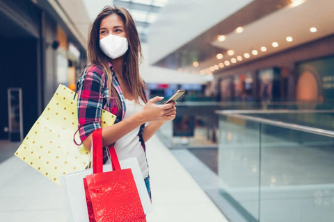 Woman in mall wearing Filtering Barrier Face Covering AFFM-5 One Size 5-Pack with stretchable side bands, holding shopping bags.