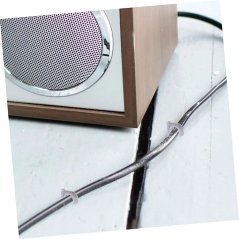 100 Pcs Wire Staples And Cable Clips With Steel Nails PE Material securing a cable on a white floor, next to a wooden speaker.