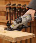 Inequalit gray mini circular saw, corded compact tool cutting wood on a workbench.
