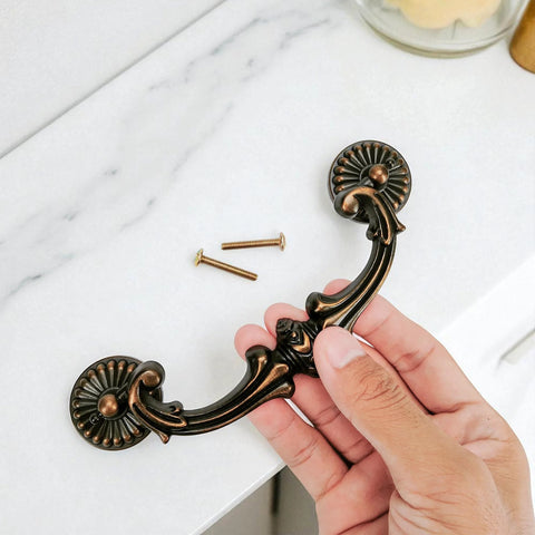 Hand holding Drop Bail Drawer Pull 5 Inch Center To Center 128 Mm Hole Spacing Includes 2 Screws Antique Brass Finish Floral Design