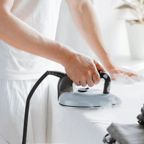 Person ironing with heavy duty high temperature steam hose for steam irons and high pressure ironing, durable tubing visible.