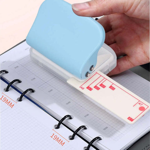 Hand using Three Hole Paper Punch Handheld Office And School Multi Size Puncher with 5.5mm holes and 19mm spacing on a notebook