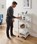 Man organizing the White 4 Tier Rolling Kitchen Cart With Pull Out Shelf Adjustable Middle Racks And Secure Locking Wheels.