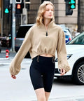 Person wearing a beige cropped sweatshirt with black cycling shorts walking in an urban setting.
