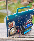 AM FM Radio Kit For DIY Soldering Projects And Electronics Teaching Hands On STEM Gift Dope Stereo Receiver Complete Parts Kit With Full Color Manual Upgraded VT-16 Version Easy Build For Beginners showing back circuit board and speaker assembly outdoors.
