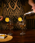 Pouring from Boss Level Heavy Duty Double Wall Vacuum Insulated Cocktail Shaker Bottle into two glasses with garnished lemon.