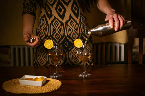 Pouring from Boss Level Heavy Duty Double Wall Vacuum Insulated Cocktail Shaker Bottle into two glasses with garnished lemon.