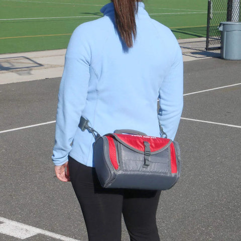 First aid kit duffel bag in red and gray carried at hip by person in blue jacket.