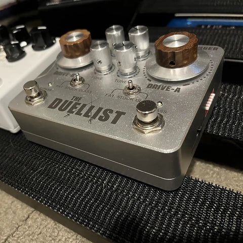 The Duelist guitar pedal with metal housing, volume and tone controls, displayed on a pedalboard.