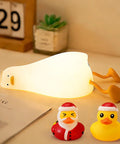 Squishy Silicone Rubber Duck Night Light For Nursery Baby And Kids Dimmable Rechargeable Touch Led Lamp BPA Free Non Toxic Bedside Light For Breastfeeding Shatterproof Safe Cozy Glow glowing on a table with two small duck figures.