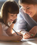Smiling child drawing in a notebook with an adult assisting, using charcoal pencils for drawing set 10 pack.