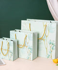 Three floral paper bags, small to large, with yellow rope handles on a table, matching the Blue Paper Bags Set Of 30 Premium 3D Cut Totes For Shopping Clothing Jewelry And Souvenirs Includes 10 Small 10 Medium 10 Large Great For Grab And Go Gifts And DIY Packaging.
