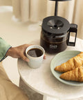 Breakfast table with 1.25L Glass Carafe for KBG Brewers, Clear Black Version, coffee, and croissants.