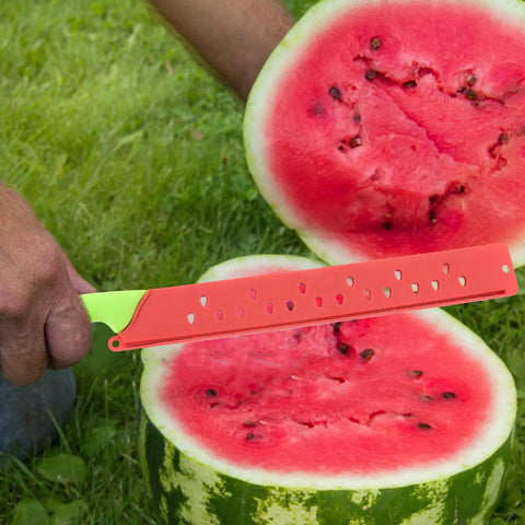 Person using Watermelon Cutter With Sleeve Long Serrated Knife to slice a watermelon outdoors on grass, showing serrated blade and handle