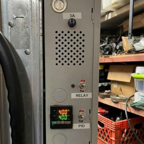 Control panel showing relay and PID display with adjustable knob, designed for electronic systems, located in a garage.