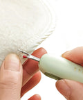 Close-up of Two-In-One Sewing Needle Threader And Seam Ripper in use, showing green tool cutting thread on fabric edge.