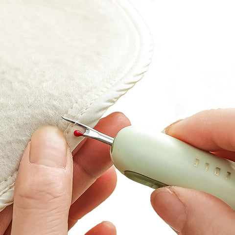 Close-up of Two-In-One Sewing Needle Threader And Seam Ripper in use, showing green tool cutting thread on fabric edge.