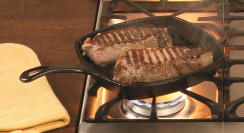 Square Cast Iron Grill Pan 10.5 Inches Preseasoned Square Skillet With Ridged Grill Surface For Burger Searing And Boss Level At Home Sear With Steakhouse Grill Marks, Even Heat Distribution PFAS Free Non Toxic Cookware For Home Grilling with steaks searing on a stovetop.