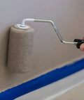 Duck Brand Clean Release painter's tape being applied with a small roller on a wall; blue tape along baseboard.