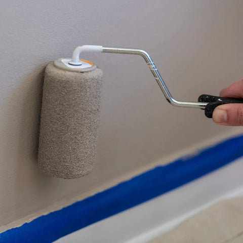 Duck Brand Clean Release painter's tape being applied with a small roller on a wall; blue tape along baseboard.