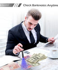 Man using 365Nm UV Flashlight Beast Power Black Light for checking banknotes on a desk with coffee and documents.
