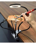 Third Hand Desk Clip Soldering PCB Holder Tool With 3X LED Magnifier in use on wooden table, showing adjustable gooseneck arms.