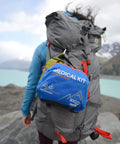 Adventure Medical Kits Mountain Series Backpacker Medical Kit blue/orange attached to a gray hiking backpack, side view