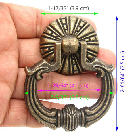 Close-up of a vintage brass ring pull handle with dragon head motifs, hand-held, showing detailed engravings and pumpkin style disk base.