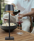 Rechargeable Cordless LED Desk Lamp with Lightweight Aluminum Body on outdoor table with wine glasses and popcorn